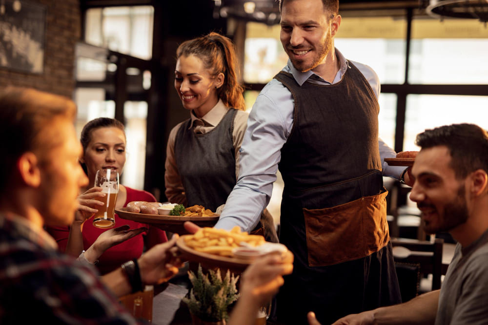 garcons-felizes-trazendo-comida-a-mesa-e-servindo-grupo-de-amigos-em-um-restaurante